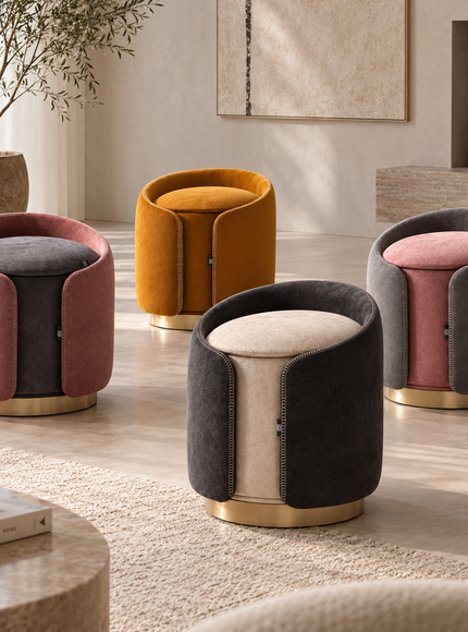 Four modern velvet barrel ottomans with curved side panels and round gold-tone bases are arranged in a bright, neutral-toned living room. The stools come in color combinations of dusty pink and dark gray, mustard yellow and dark brown, and light beige and dark gray.