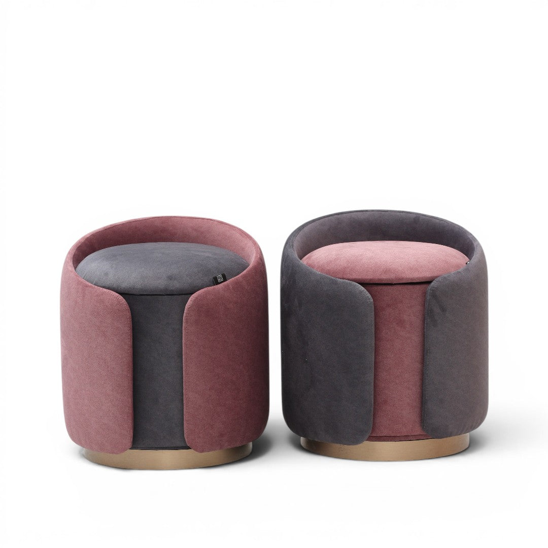 Two modern velvet ottomans with rounded cylindrical shapes in dusty pink and dark gray, featuring gold-toned wooden bases. 
