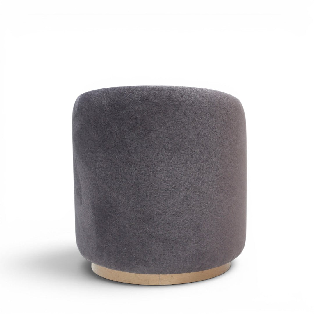 A cylindrical upholstered ottoman or stool in dusty grey velvet, featuring a light natural wood base, shown against a plain white background.