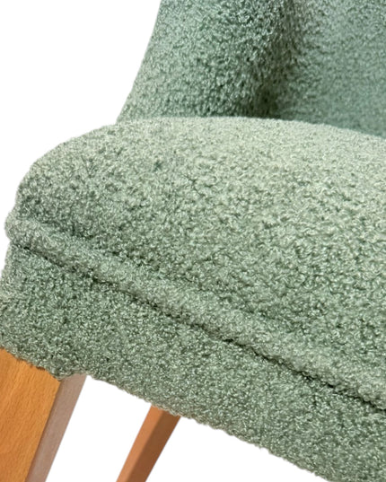 Modern green bouclé accent chair with wooden legs and curved backrest, showcasing a soft textured finish and minimalist arm design