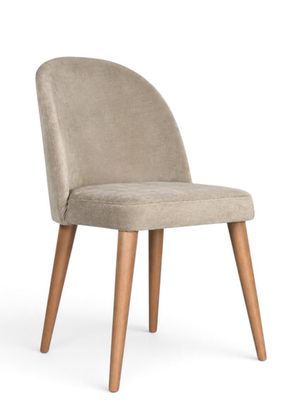 A modern dining chair with a curved backrest upholstered in light beige velvet, supported by four tapered natural wood legs, shown against a plain white background.