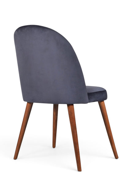 A modern dining chair with a dark slate blue velvet upholstered back and seat, supported by four tapered medium-brown wooden legs, shown from a three-quarter angle on a white background.