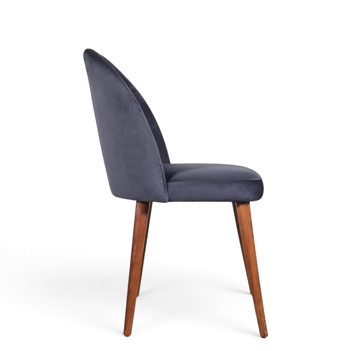 A modern dining chair with a curved back upholstered in dark blue-gray velvet, supported by four tapered medium-brown wooden legs, shown from a side profile on a white background.