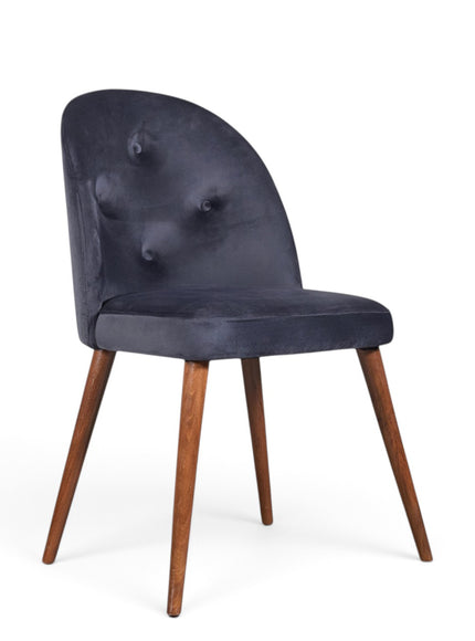 A modern dining chair with a dark navy blue velvet upholstered seat and curved backrest featuring button tufting, supported by four tapered medium-brown wooden legs, shown on a plain white background.