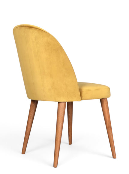 A modern dining chair with a curved back upholstered in mustard yellow velvet, supported by four tapered medium-brown wooden legs, shown from a three-quarter angle on a white background.