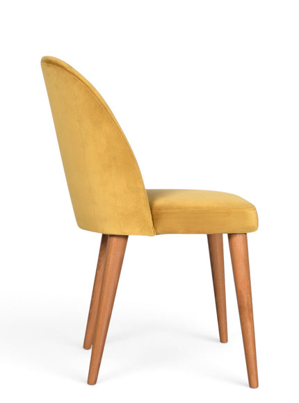 A modern dining chair with a curved back upholstered in mustard yellow velvet, supported by four tapered medium-brown wooden legs on a white background.
