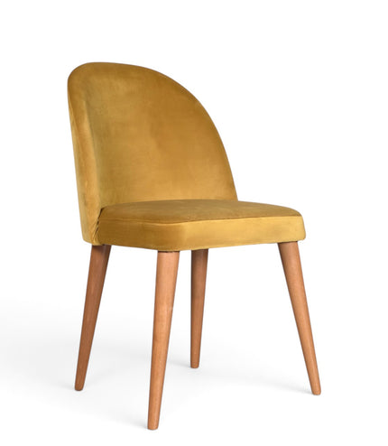A modern dining chair with a curved back upholstered in mustard yellow velvet, supported by four tapered medium-brown wooden legs on a white background.