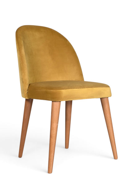 A modern dining chair with a curved back upholstered in mustard yellow velvet, supported by four tapered medium-brown wooden legs on a white background.