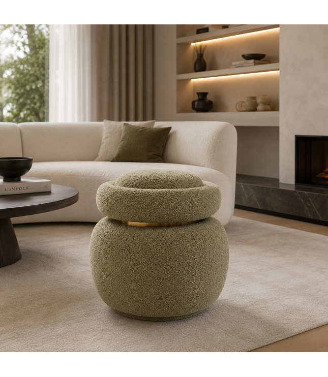 A round, low stool with a textured, bouclé-like fabric in a muted sage green, featuring a gold metallic band around its upper tier. The stool is placed in a modern living room setting on a beige rug in front of a cream-colored sofa.