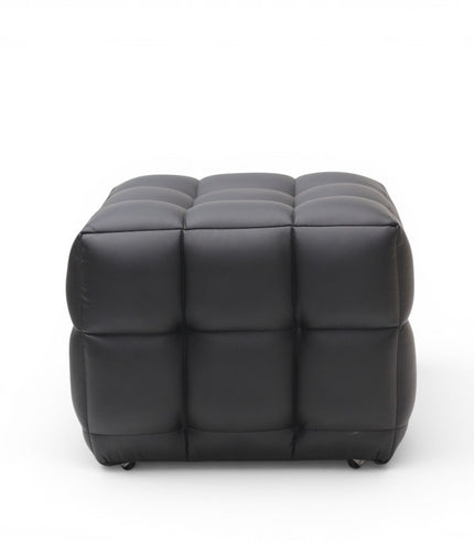 A modern black tufted cube ottoman with a padded, segmented design and small black feet, shown against a plain white background.
