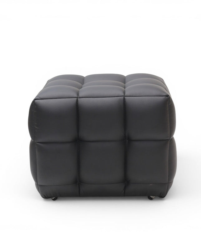 A modern black tufted cube ottoman with a padded, segmented design and small black feet, shown against a plain white background.
