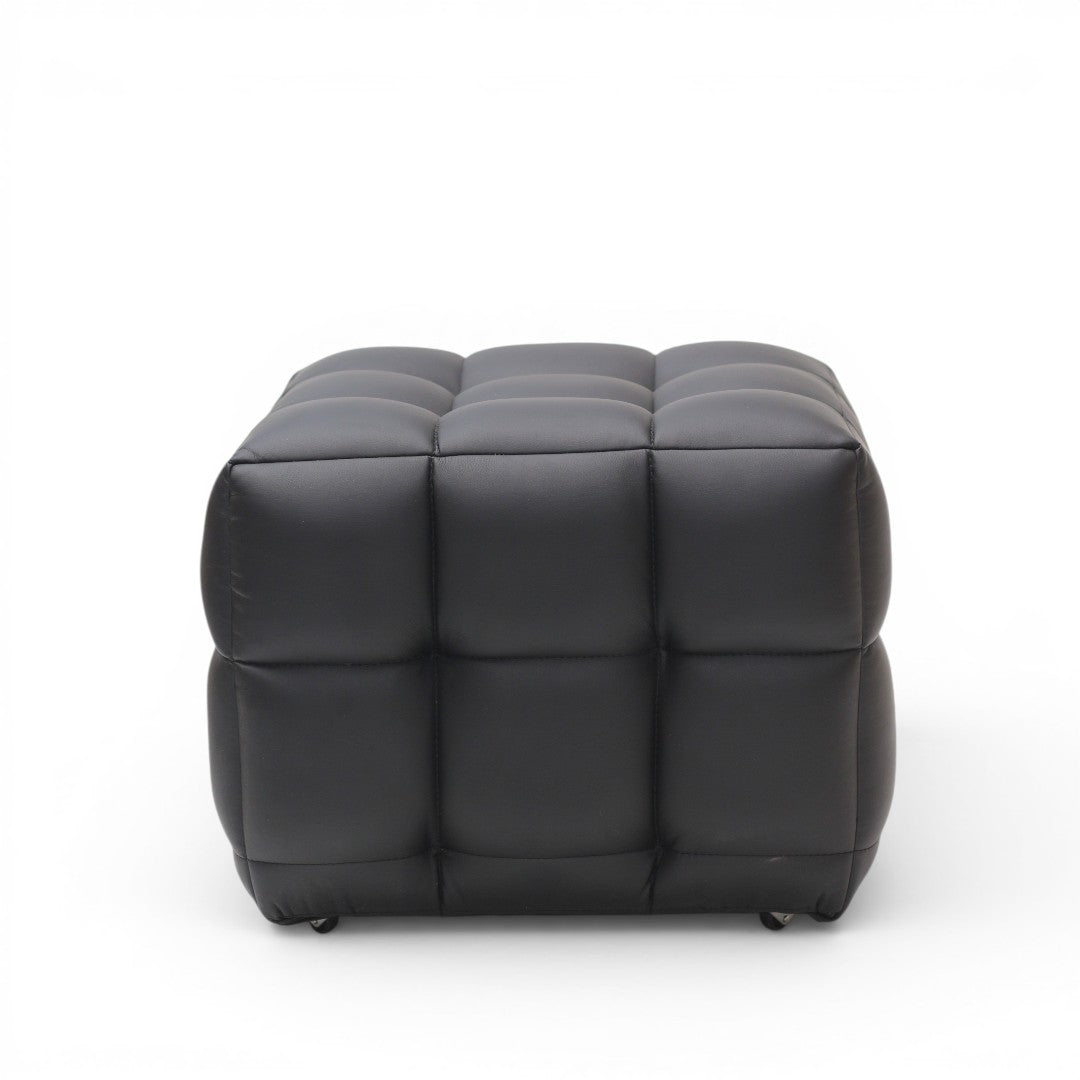 A modern black tufted cube ottoman with a padded, segmented design and small black feet, shown against a plain white background.