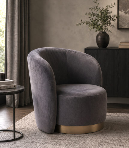 A modern barrel-style accent chair upholstered in dark gray velvet with a brushed gold metal base, set in a styled living room interior.