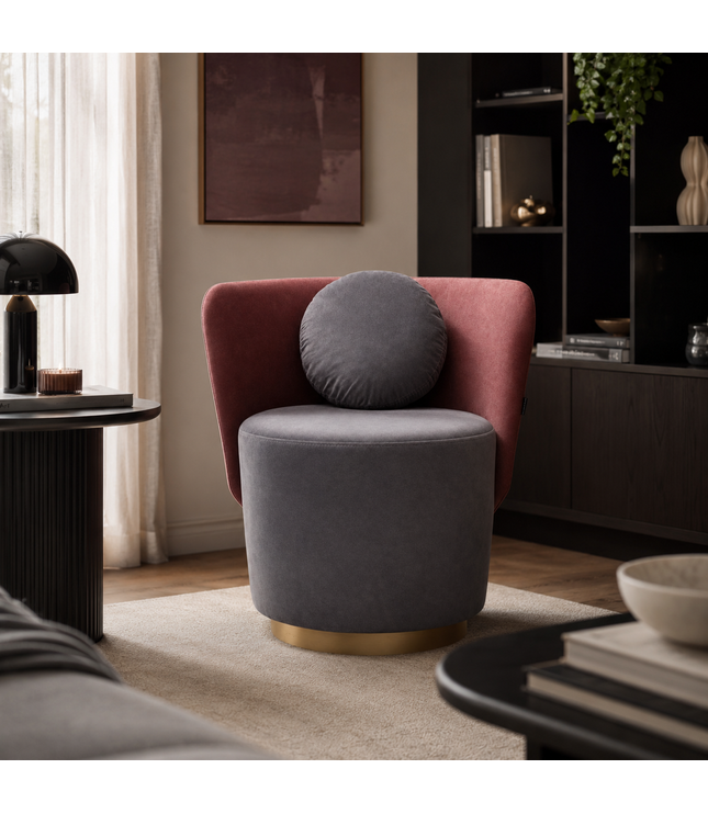 A modern accent chair in a styled living room, featuring a dusty rose velvet armchair with a round gray lumbar pillow and a cylindrical gray velvet seat on a gold-finished base.
