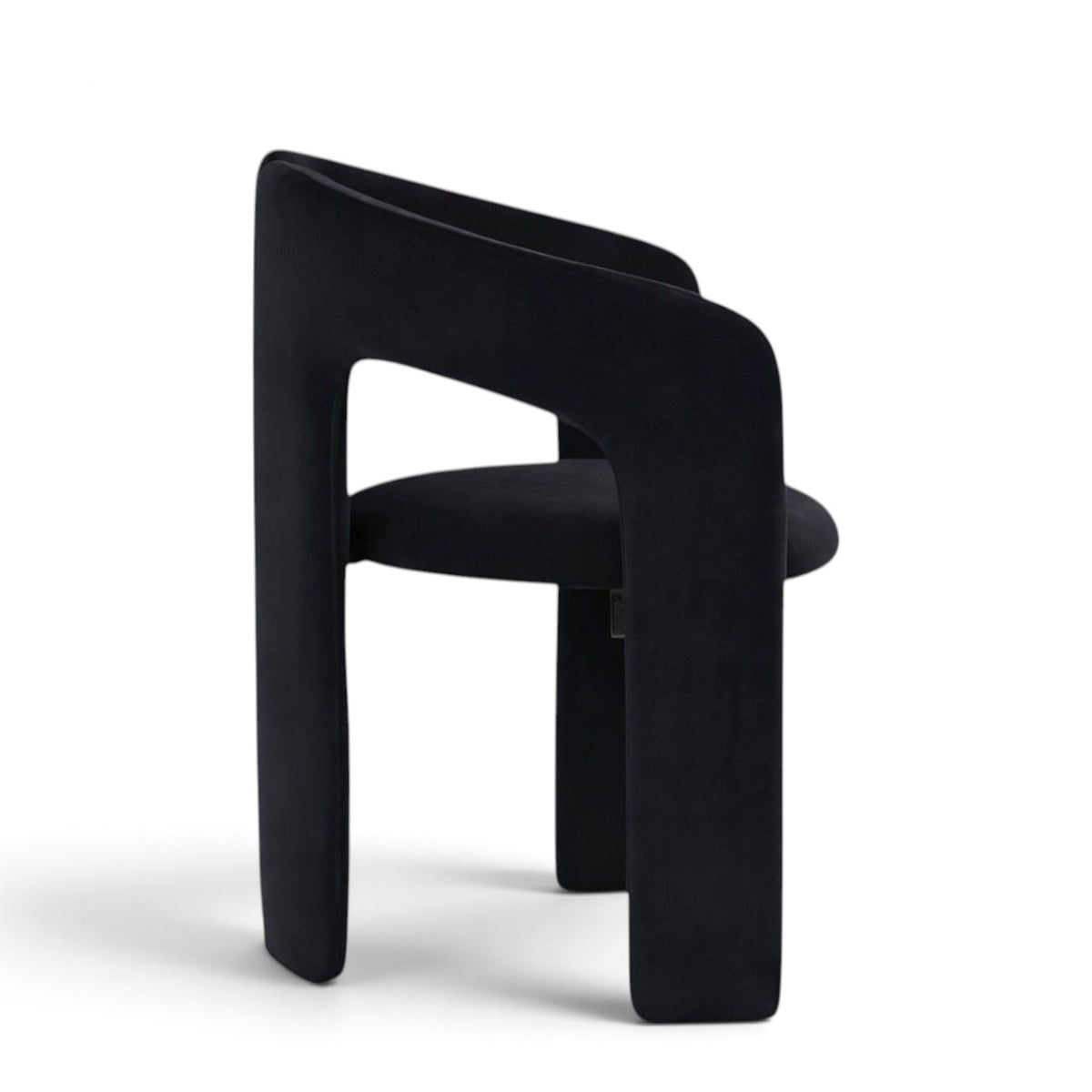 A modern black velvet dining chair with a unique split backrest and wide block legs, shown from the side on a white background.