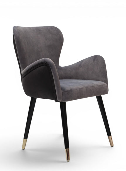 A modern gray velvet dining chair with black tapered legs and gold-toned metal tips, shown against a plain white background.