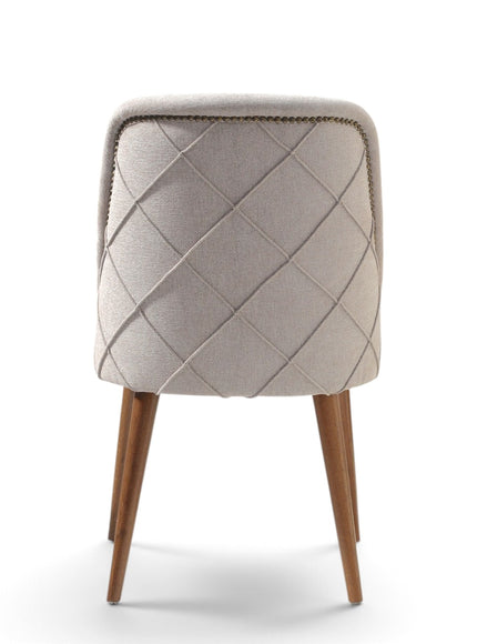 A modern upholstered dining chair with a diamond-quilted backrest in light beige fabric, supported by four tapered medium-brown wooden legs, shown against a plain white background.