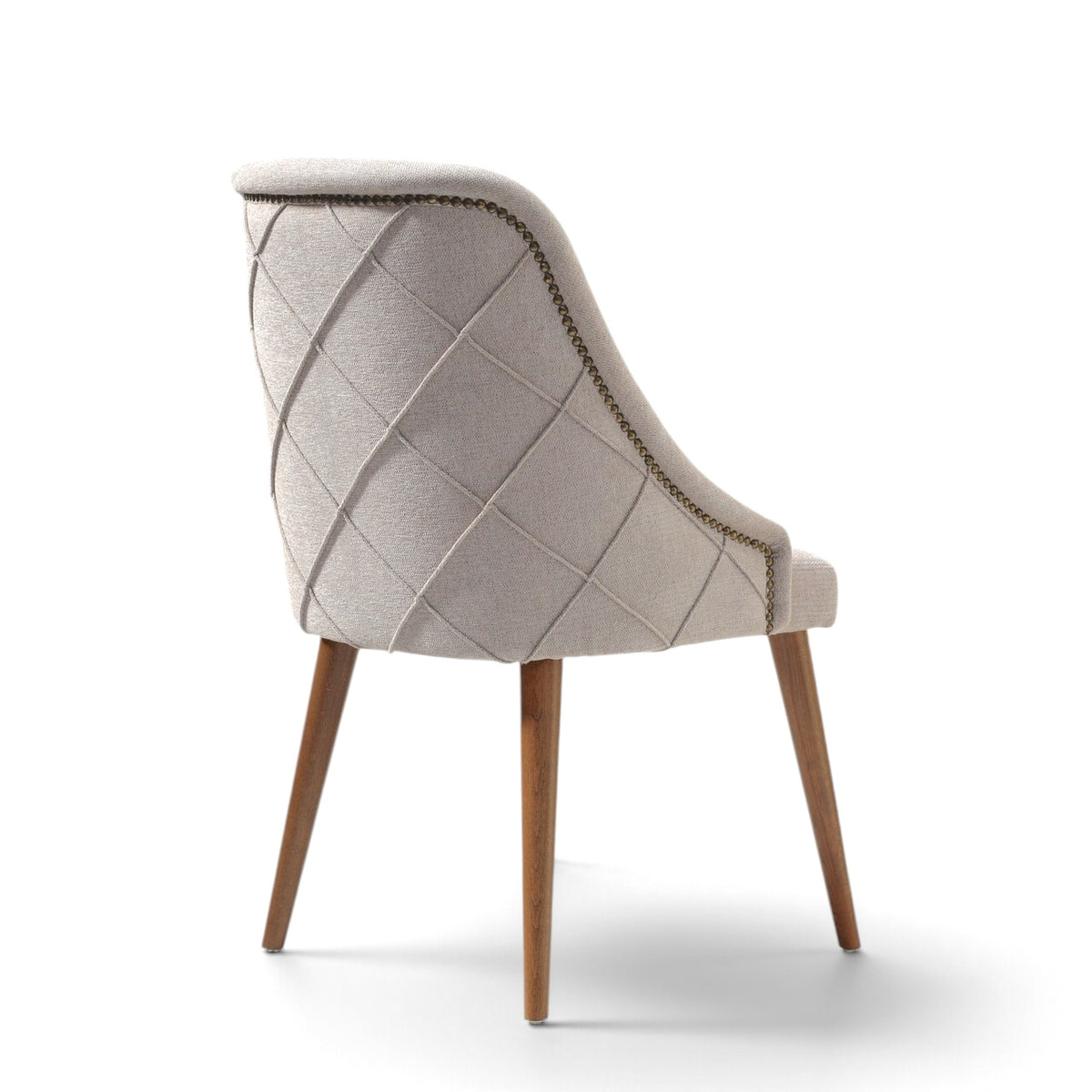 A light beige upholstered dining chair with a diamond-quilted pattern on the backrest, wooden legs, and brass nailhead trim, shown from a three-quarters angle on a white background.