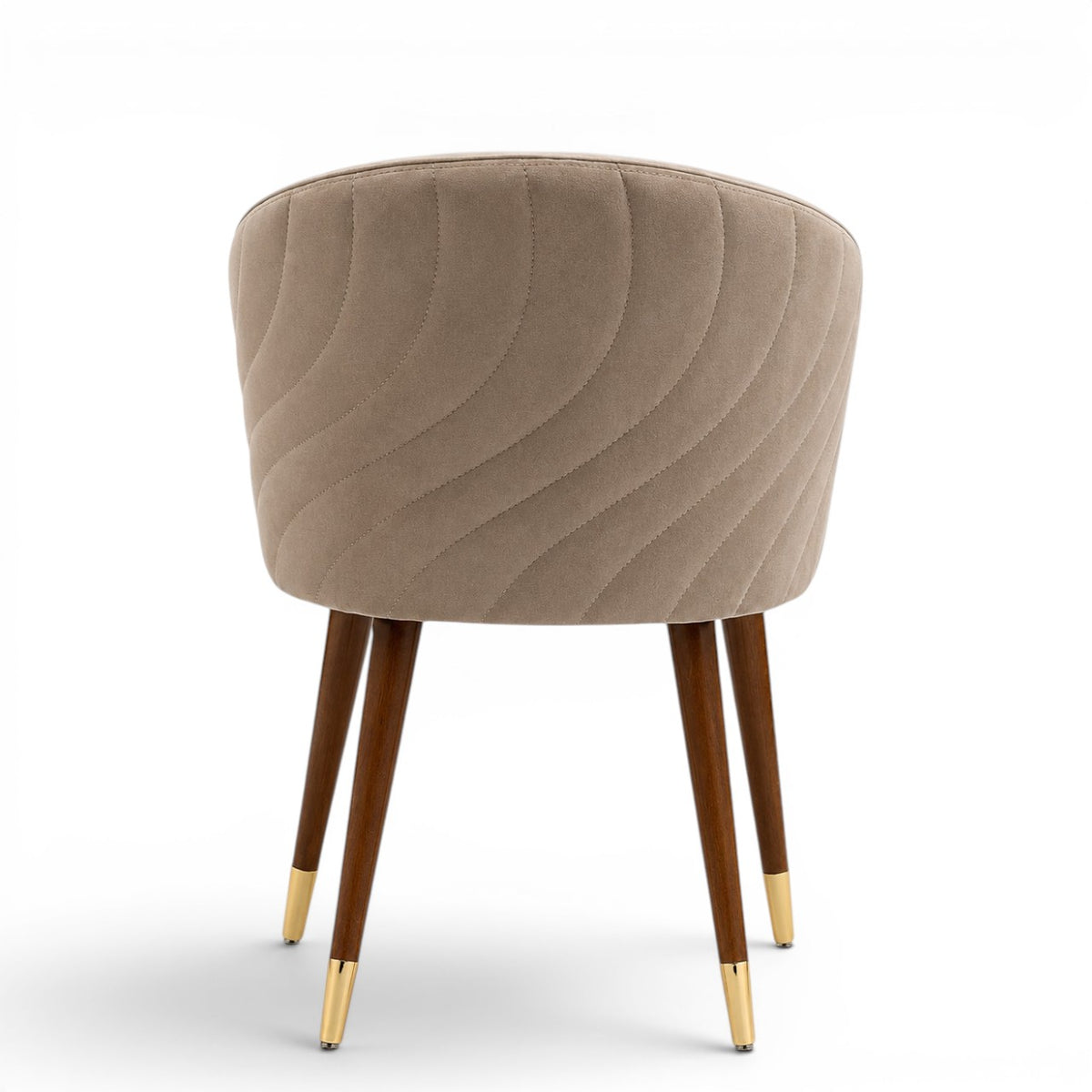 A modern barrel-style dining chair with a rounded, tufted backrest upholstered in taupe-beige velvet, supported by four tapered dark brown wooden legs with polished gold metal tips, shown against a plain white background.
