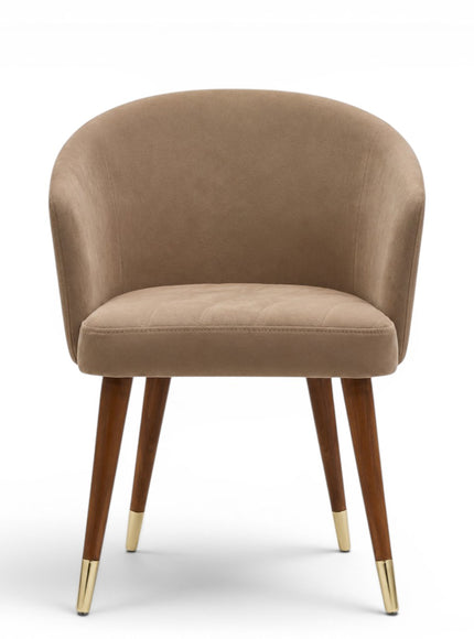 A modern dining chair with a curved, tufted backrest and seat upholstered in a warm taupe-beige fabric, supported by four tapered dark brown wooden legs with gold metal caps, shown against a plain white background.