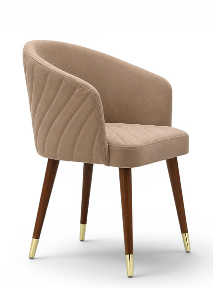 A modern dining chair with a curved, tufted backrest and seat upholstered in a warm taupe-beige fabric, supported by four tapered dark brown wooden legs with gold metal caps, shown against a plain white background.