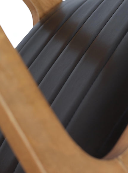 Close-up of the Vaya Home Abre dining chair showing the black channel-stitched seat and wood frame detail.