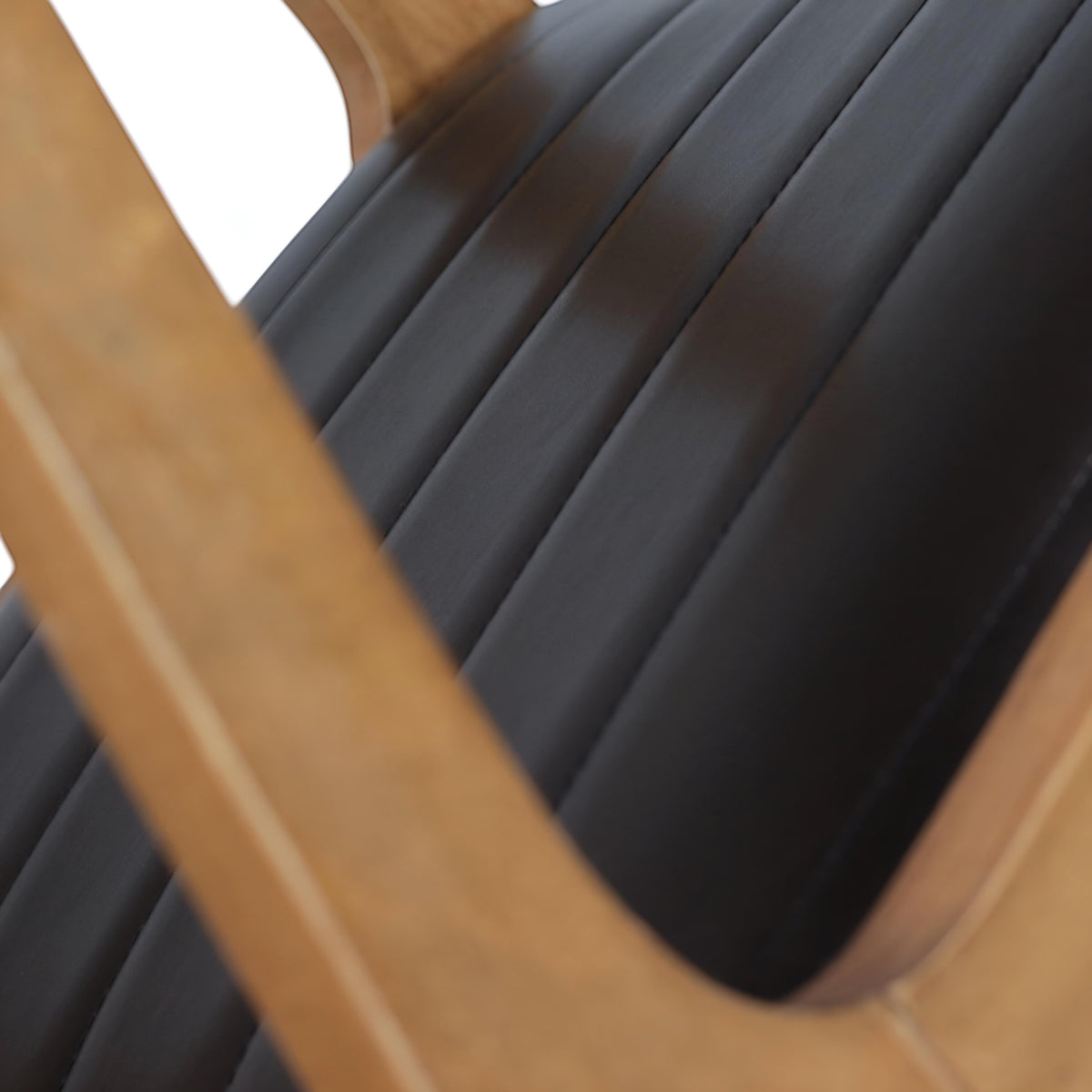 Close-up of the Vaya Home Abre dining chair showing the black channel-stitched seat and wood frame detail.