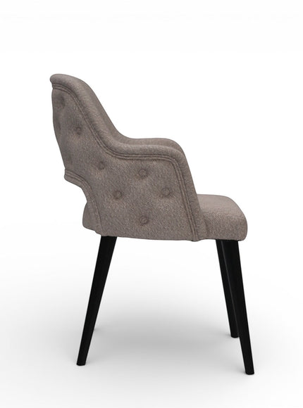 Side view of the Vaya Home Alt dining chair featuring beige upholstery, curved arms, button-tufted outer back, and black tapered legs.