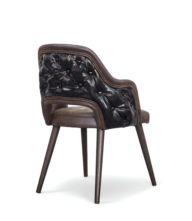 Rear angled view of the Vaya Home Alt dining chair with dark brown leather upholstery, button-tufted outer back, curved arms, and tapered wood legs.