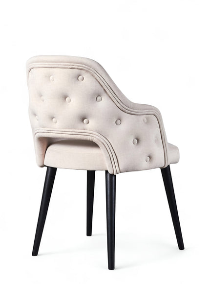 Rear angled view of the Vaya Home Alt dining chair with white upholstery, button-tufted outer back, curved arms, and black tapered legs.