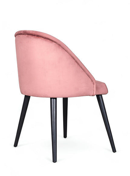Rear angled view of the Vaya Home Alveare dining chair featuring pink upholstery and black tapered legs.