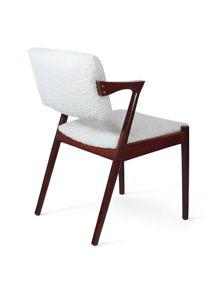 Rear angled view of the Vaya Home Angolo dining chair featuring white boucle upholstery, angled wood arms, and a dark wood frame.
