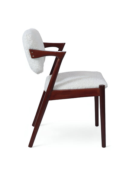 Side view of the Vaya Home Angolo dining chair with white boucle upholstery, angled wood arms, and a dark wood frame.