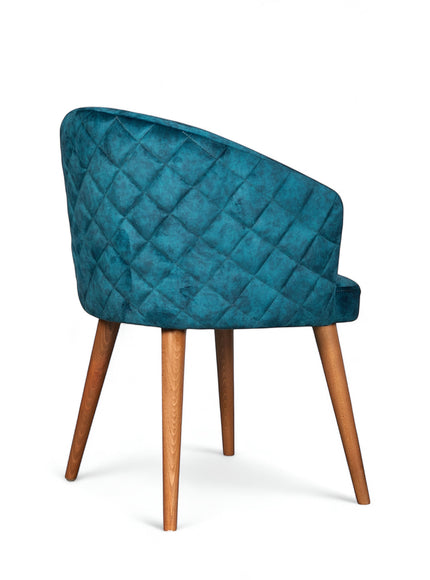 Rear angled view of the Vaya Home Antigo dining chair featuring blue velvet upholstery, diamond-quilted back detail, and tapered wood legs.