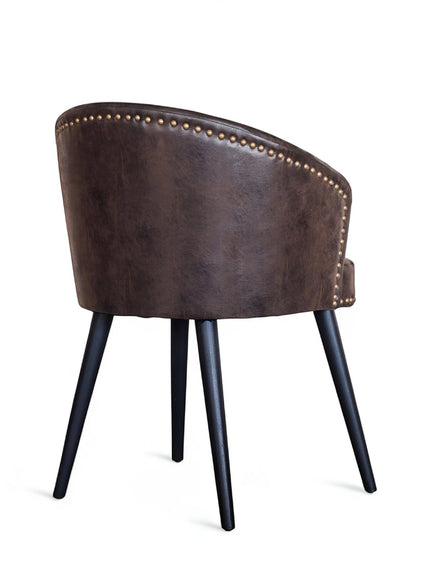 Rear angled view of the Vaya Home Antigo dining chair with dark brown leather upholstery, nailhead trim, barrel back, and black tapered legs.