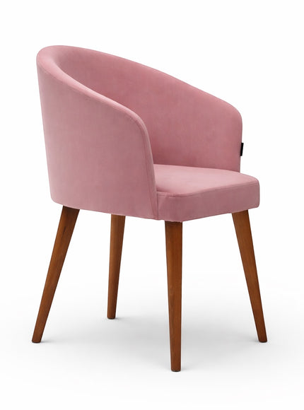Front angled view of the Vaya Home Antigo dining chair with pink velvet upholstery, curved barrel back, and tapered wood legs.