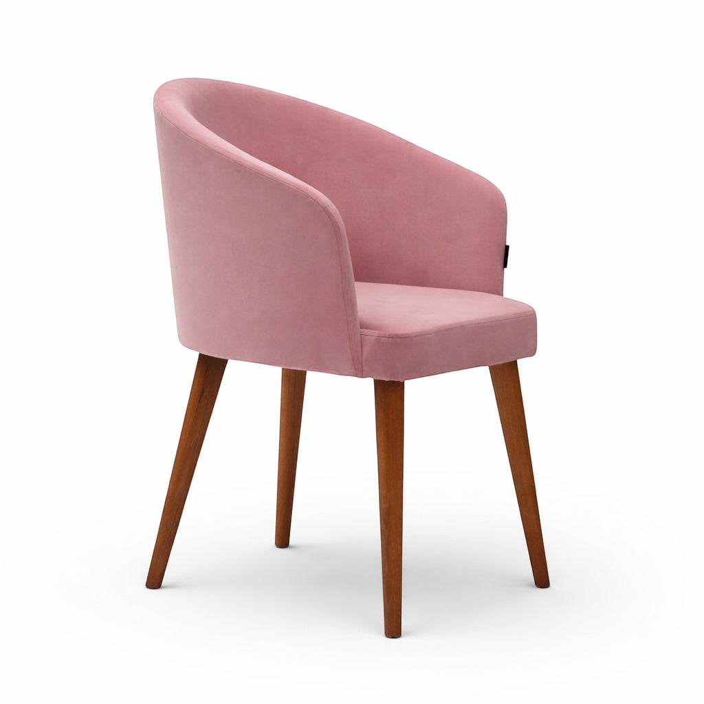 Front angled view of the Vaya Home Antigo dining chair with pink velvet upholstery, curved barrel back, and tapered wood legs.