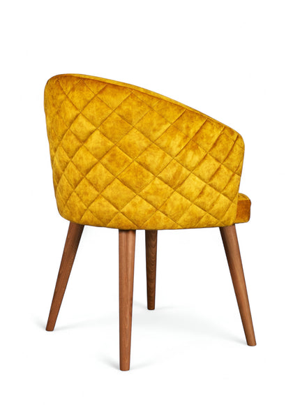 Rear angled view of the Vaya Home Antigo dining chair featuring yellow velvet upholstery, diamond-quilted back detail, and tapered wood legs.