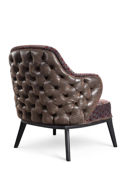 Rear angled view of the Vaya Home Array accent chair with a button-tufted brown leather back, patterned seat and inner back, and black legs.