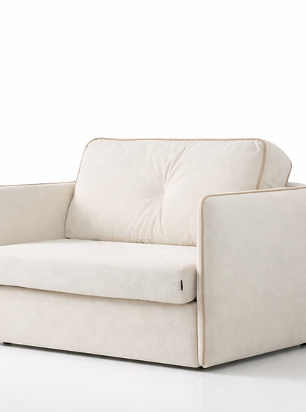 Angled view of the Vaya Home Aureo sleeper chair featuring cream boucle upholstery, cushioned backrest, and piped trim.