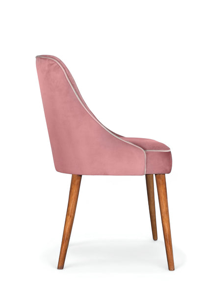 Rear angled view of the Vaya Home Azzurro dining chair featuring pink upholstery, a softly curved backrest, and tapered wood legs.