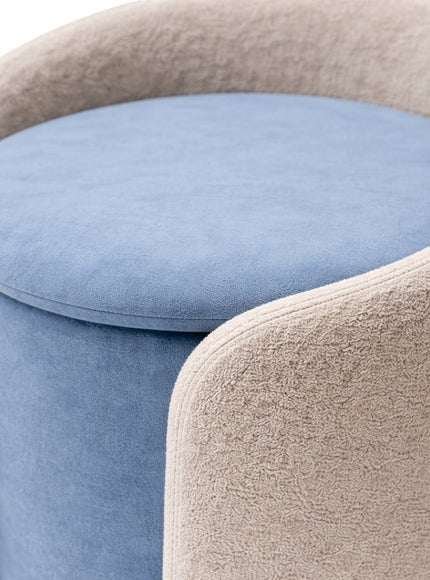 Close-up of the Vaya Home Barrel storage ottoman featuring a blue cushioned seat and light cream outer upholstery.