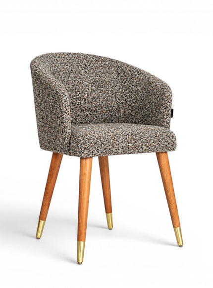 Front angled view of the Vaya Home Cambria accent chair with multitone textured upholstery, a rounded barrel back, and tapered wood legs with gold caps.