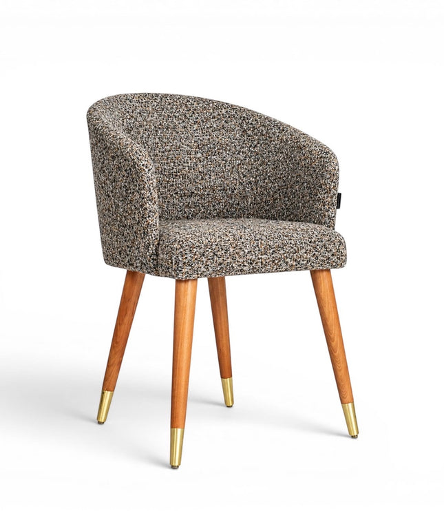 Front angled view of the Vaya Home Cambria accent chair with multitone textured upholstery, a rounded barrel back, and tapered wood legs with gold caps.