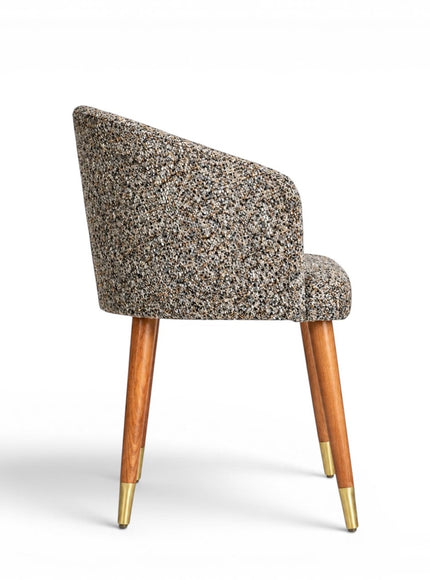 Side view of the Vaya Home Cambria accent chair featuring multitone textured upholstery, a curved backrest, and tapered wood legs with gold caps.