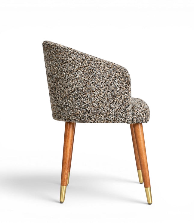 Side view of the Vaya Home Cambria accent chair featuring multitone textured upholstery, a curved backrest, and tapered wood legs with gold caps.