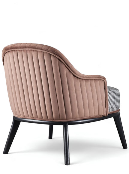 Rear angled view of the Vaya Home Carruba accent chair with a rose gold channel-tufted back, gray seat cushion, and black legs.