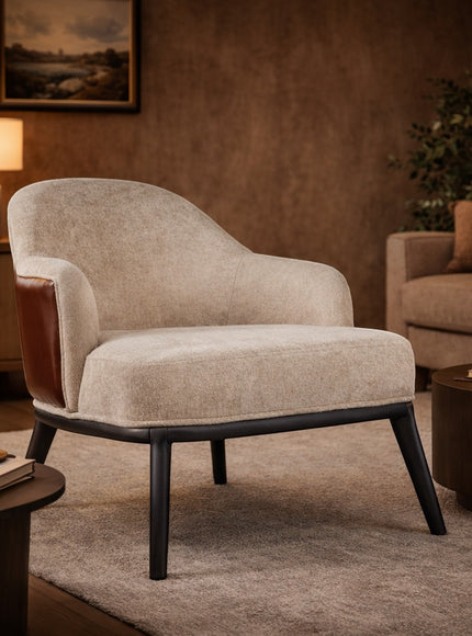 Vaya Home Chocolate accent chair with beige upholstery, brown leather outer back, and black legs, styled in a warm modern living room.