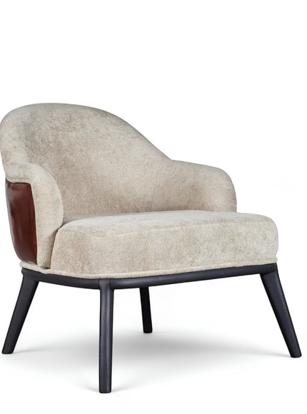 Front angled view of the Vaya Home Chocolate accent chair with beige upholstery, curved silhouette, brown leather side detail, and black legs.