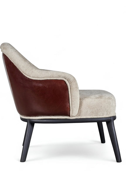 Side view of the Vaya Home Chocolate accent chair featuring beige upholstery, brown leather outer back, curved arms, and black legs.